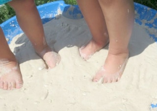 Combined cornstarch and water to make quicksand in a kiddie pool with two kids feet in the sand
