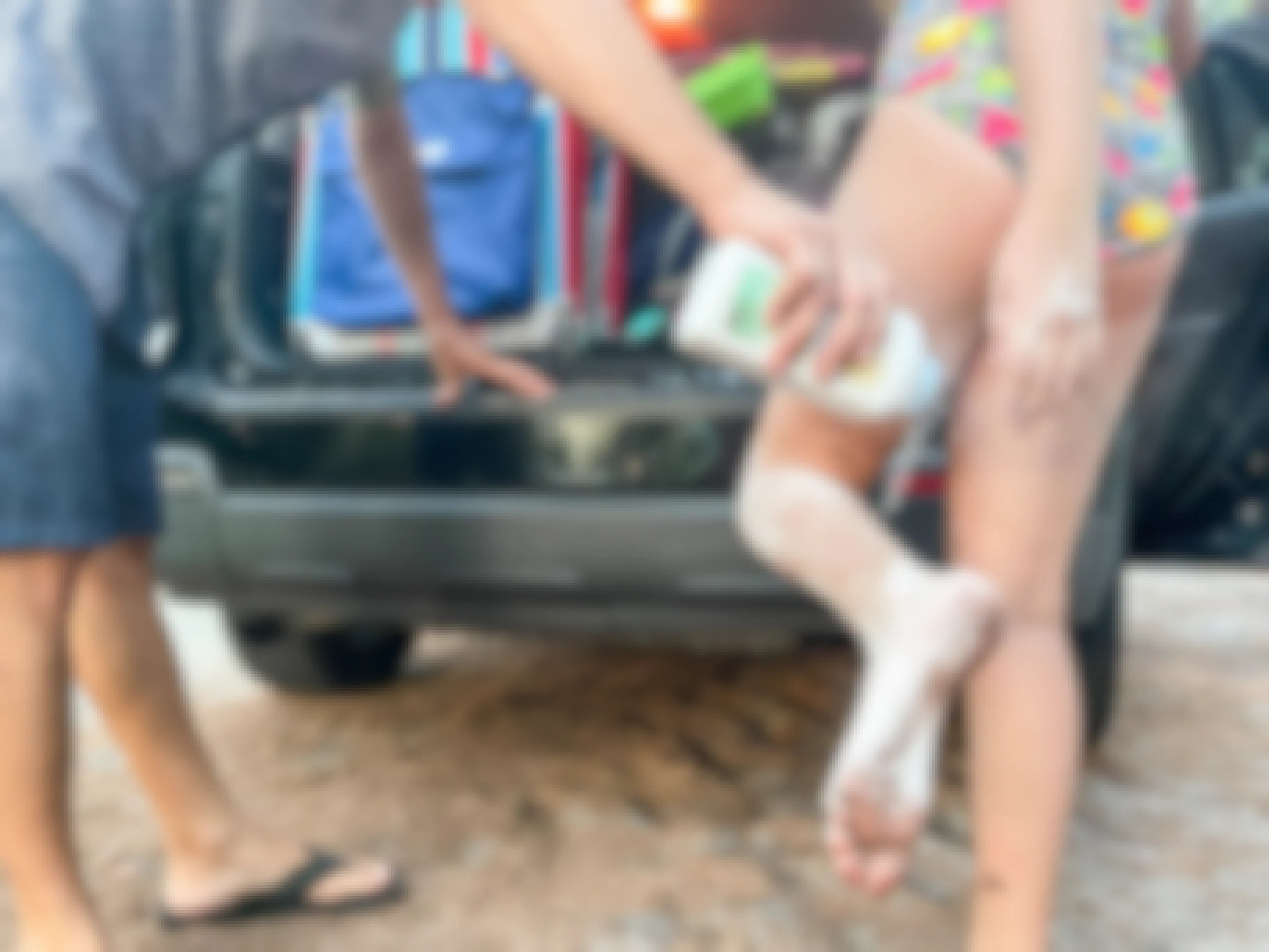 man putting baby powder on girl to get off sand on her legs next to car