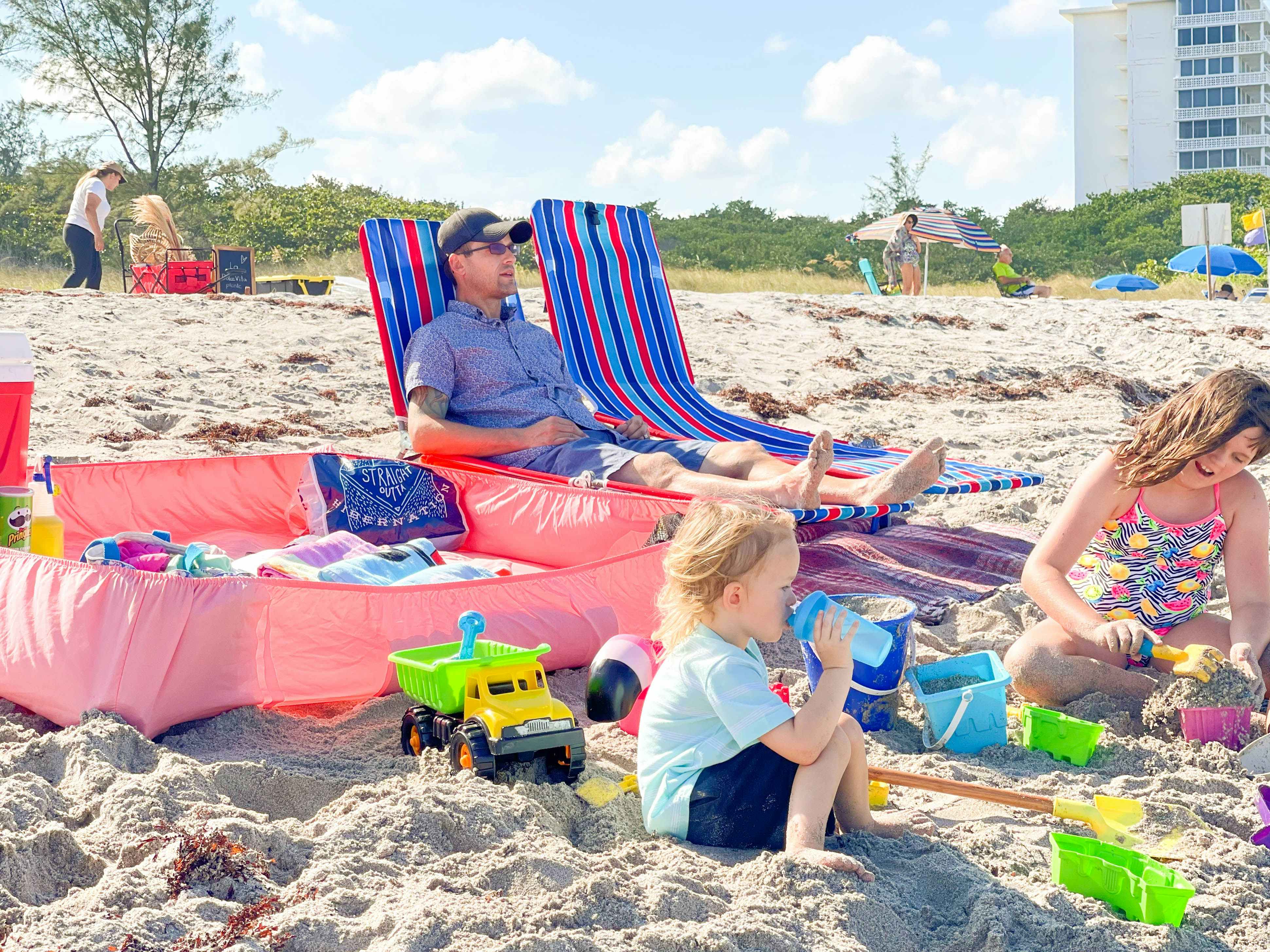 Man sitting in beach chair with to kids playing with toys in the sand
