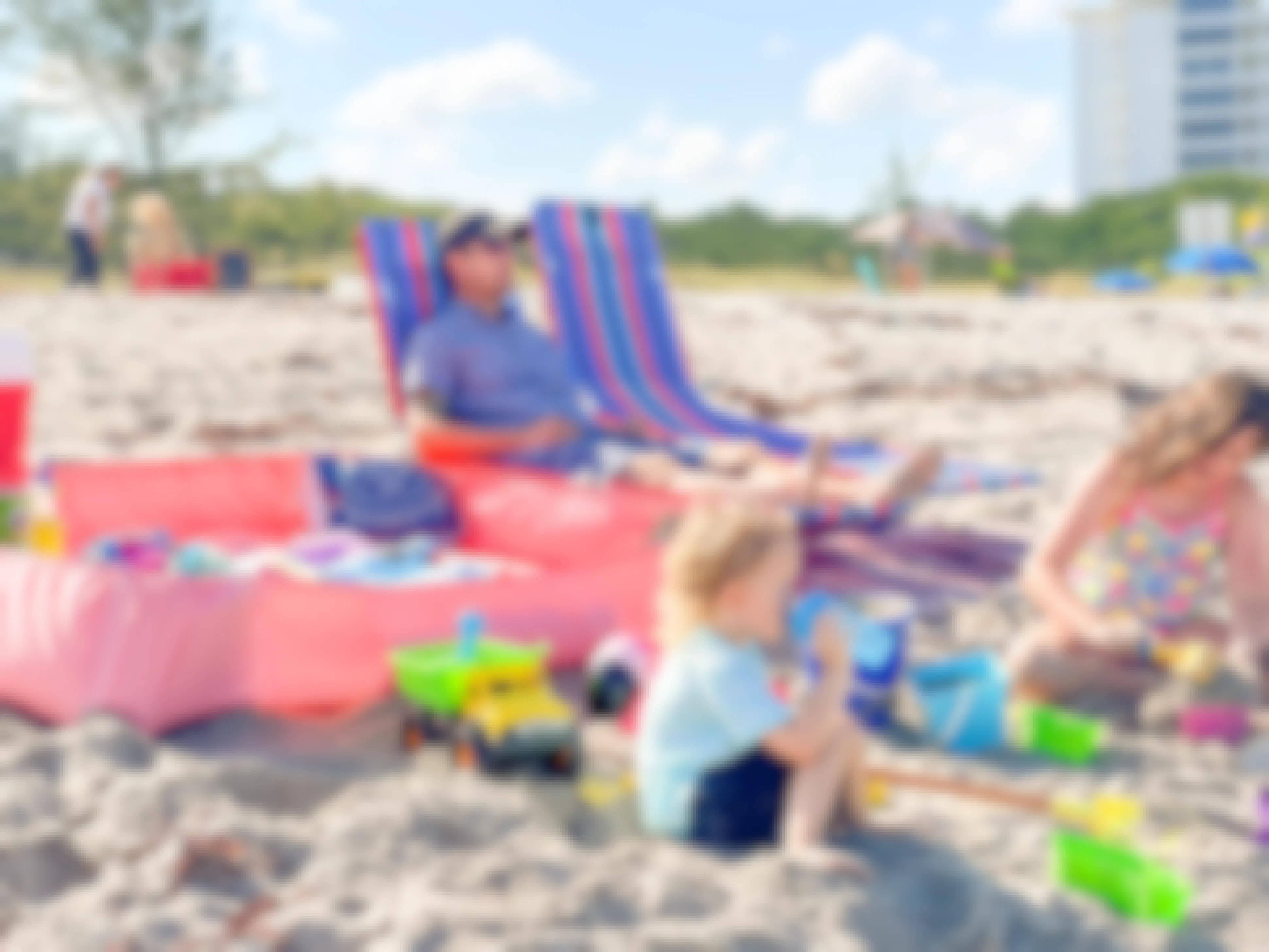 Man sitting in beach chair with to kids playing with toys in the sand