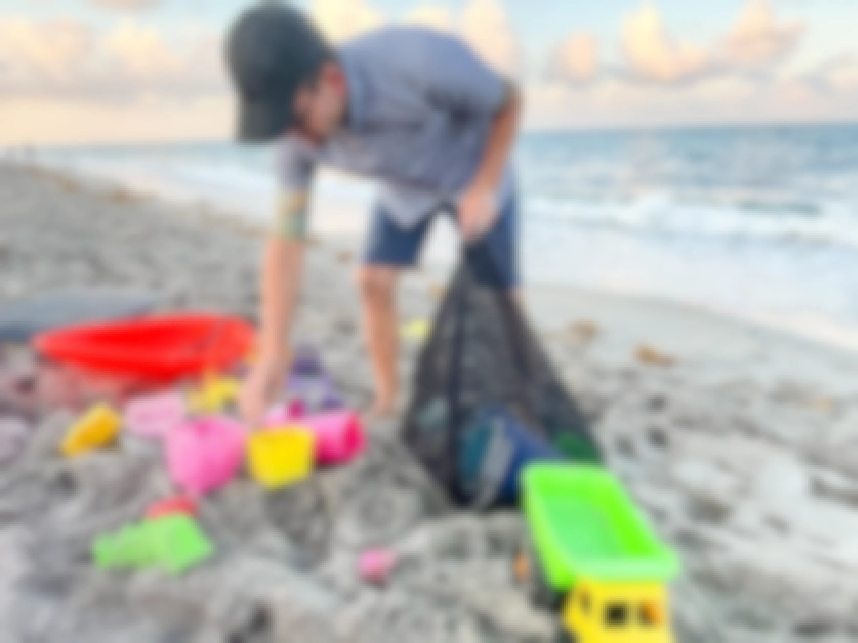 man putting beach toys in a mesh bag on the beach