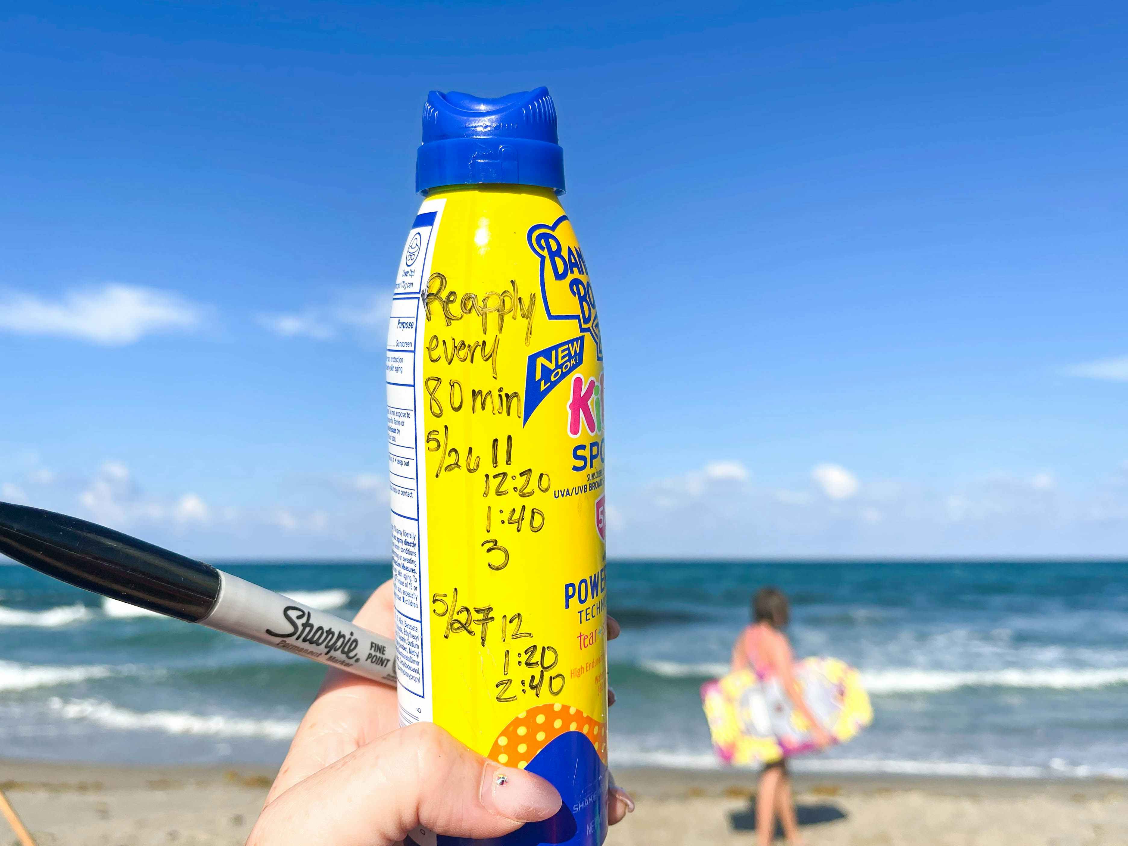 a spray bottle of sunscreen with times to reapply written in permanent marker at the beach