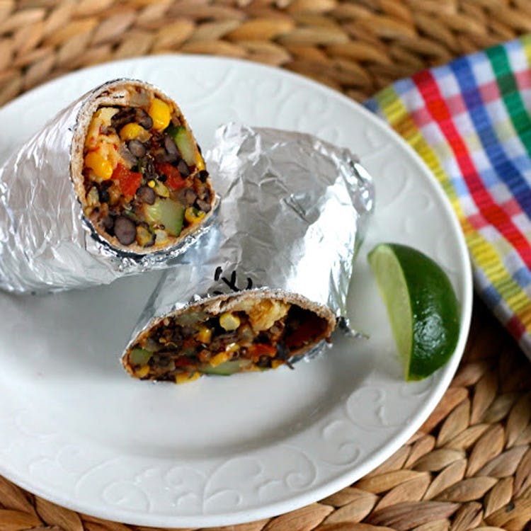 A foil wrapped burrito with a lime on a dish