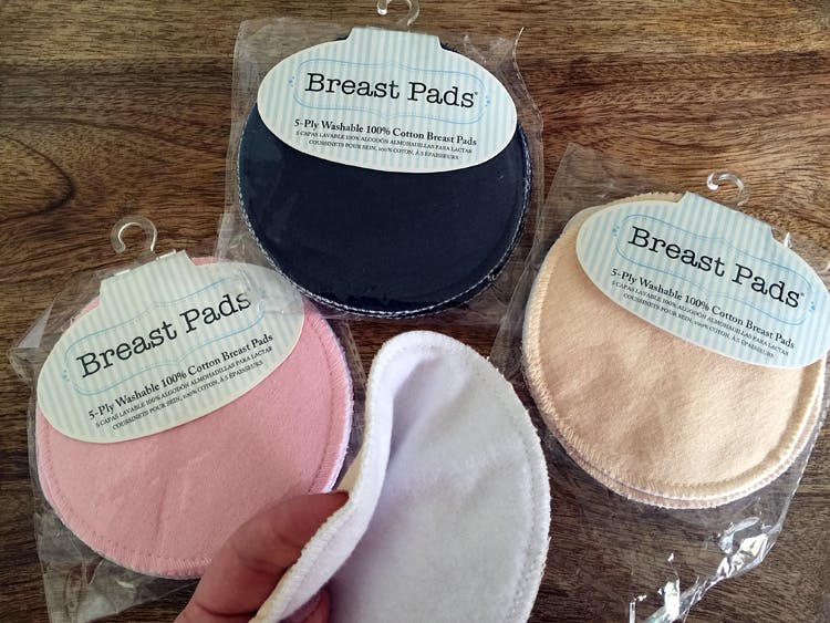 A person holding a Breast Pad above three more Breast pads in their packaging on a wooden table.