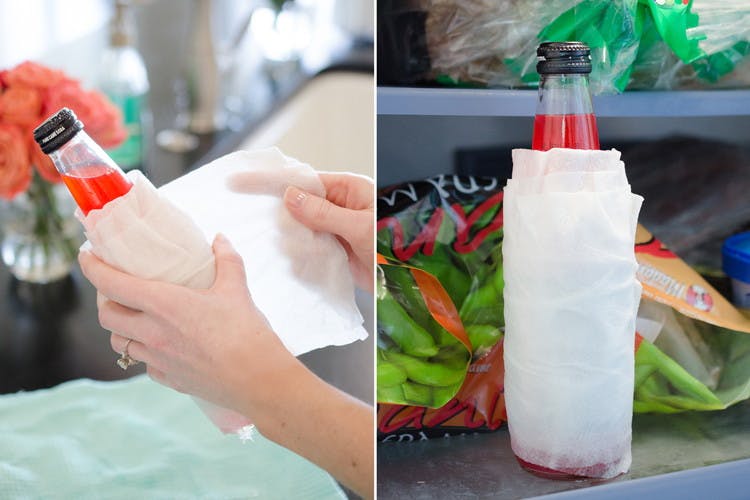 A person's hands wrapping a wet paper towel around a glass drink bottle, and the wrapped glass drink bottle sitting on the freezer shelf.