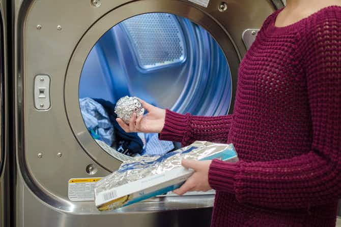 Person putting ball of Aluminum foil into a dryer with clothes