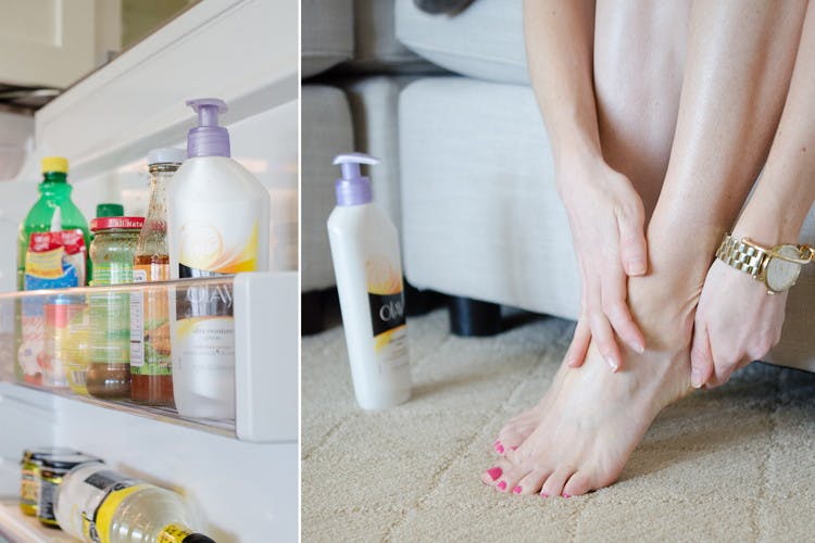 A fridge door opened with a bottle of Olay lotion on the shelf and beside that, a person sitting on a couch, reaching down to apply lotion to her feet next to the Olay lotion bottle on the ground.