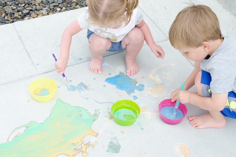 Children painting on a sidewalk with homemade paint.