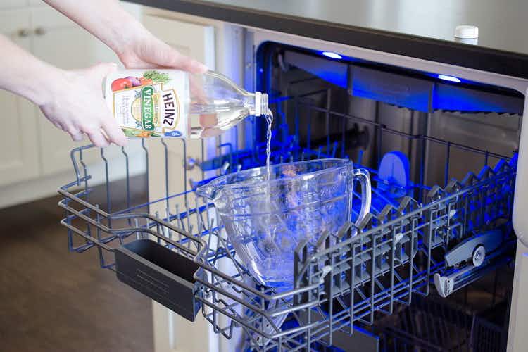someone pouring vinegar in a measuring cup in dishwasher