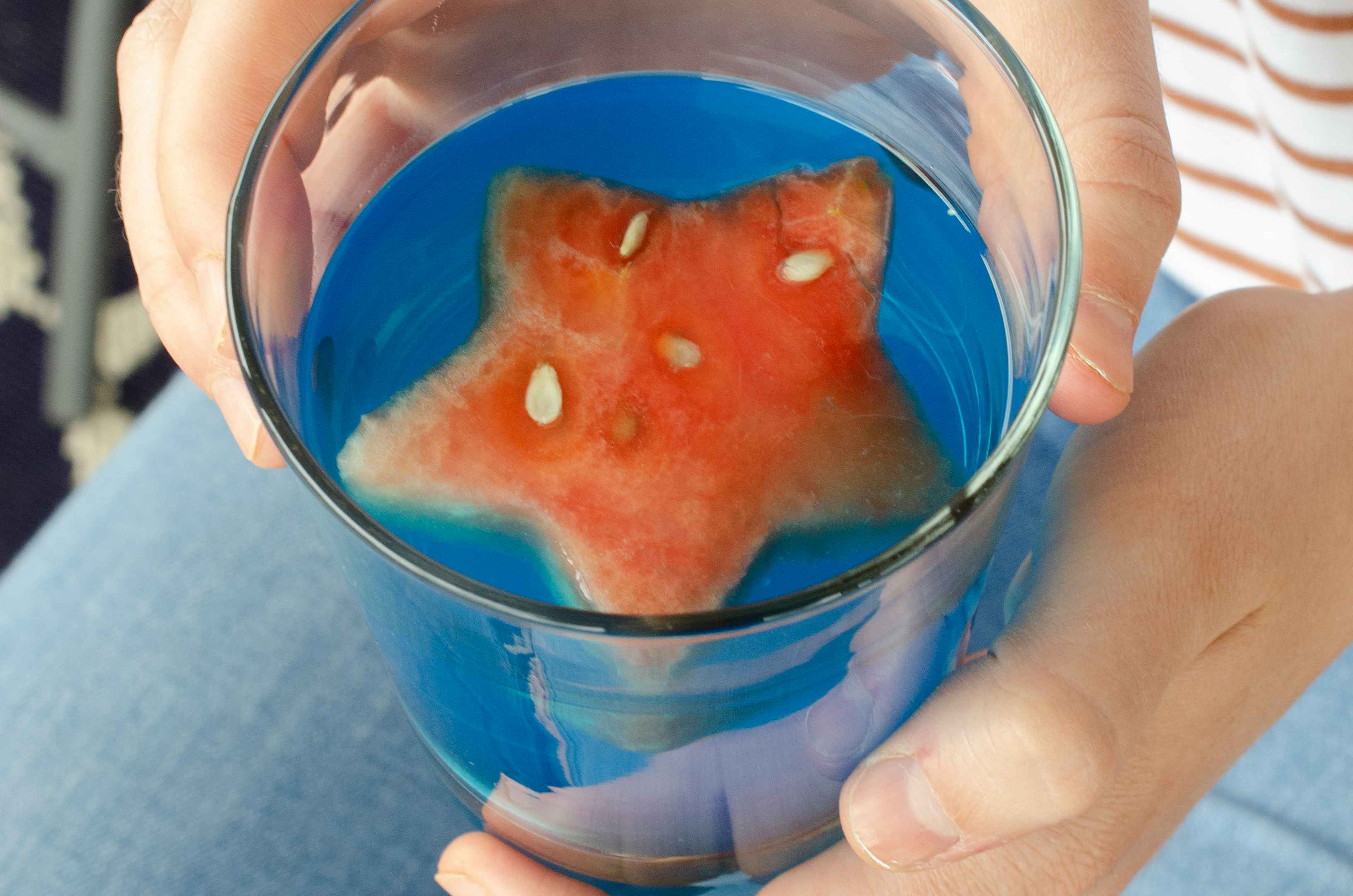 A piece of watermelon cut like a star in a blue drink glass.