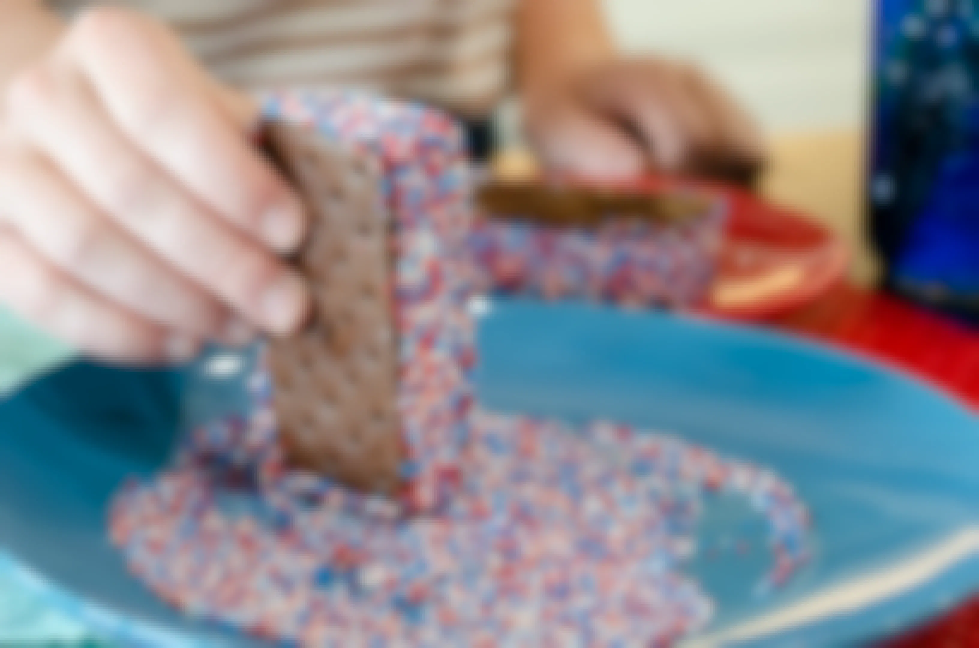 A person dipping an ice cream sandwich in red, white, and blue sprinkles.