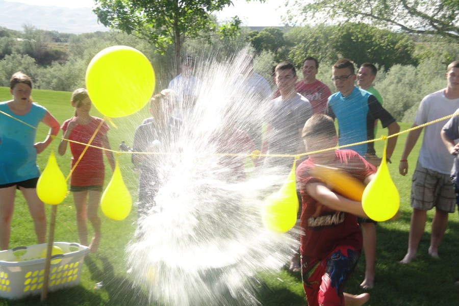A water balloon bursting next to a string of more water balloons. In the background is a group of people waiting for their turn at the water balloon piñata game. 