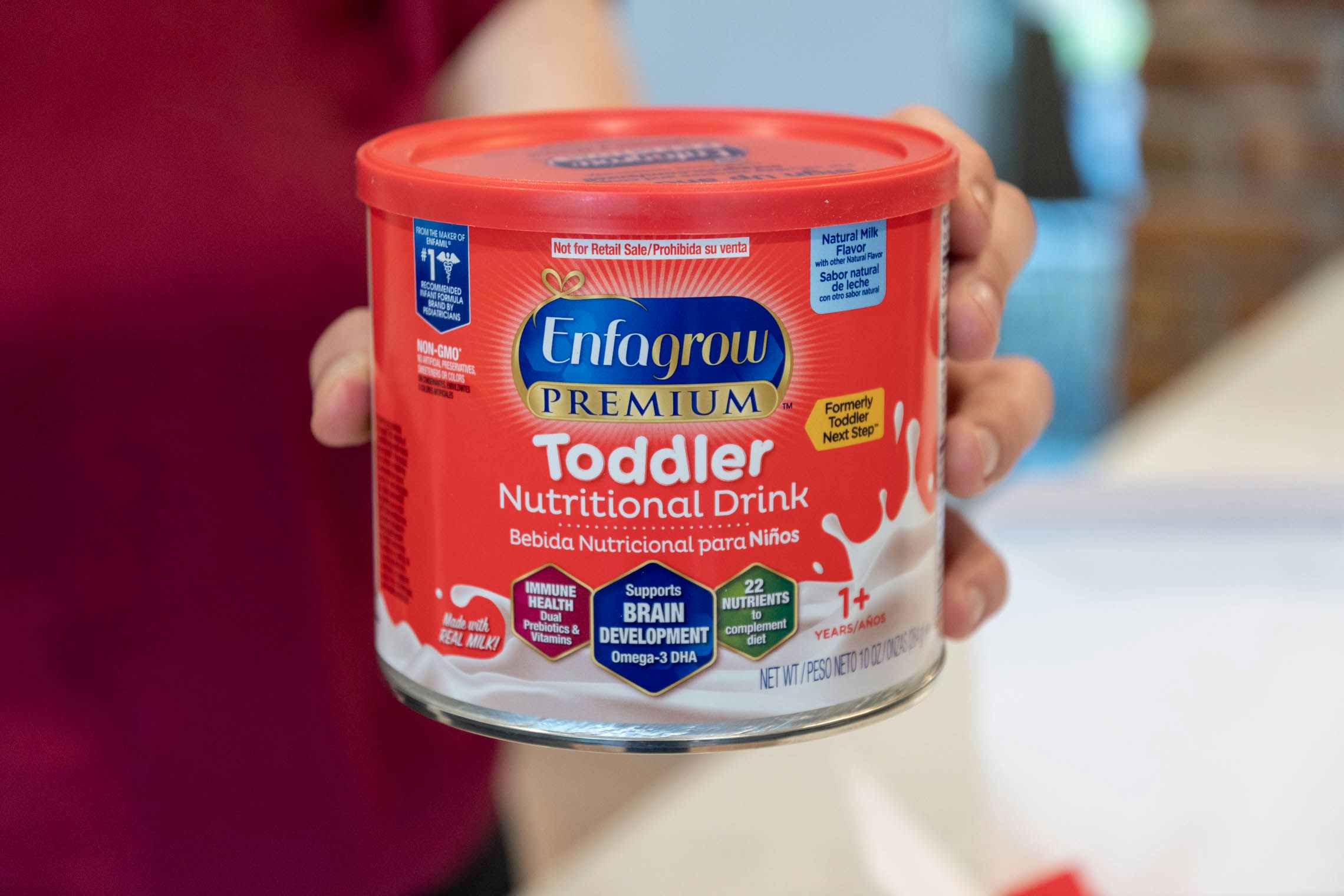 A person holding up a container of Enfagrow toddler nutritional drink in a kitchen.