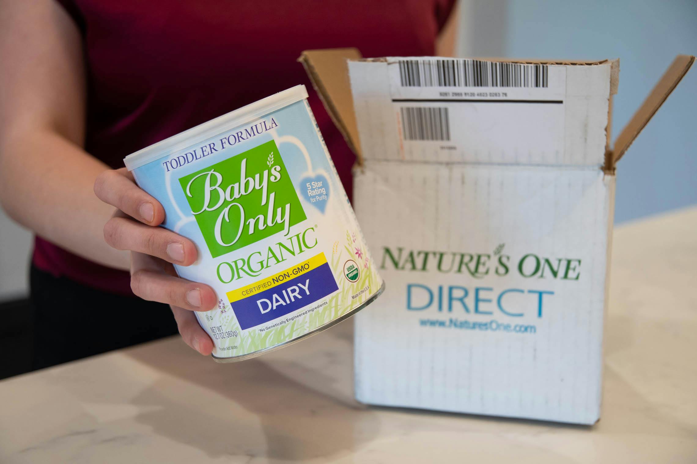A person holding a canister of Baby's Only toddler organic formula in front of a Nature's One Direct box..
