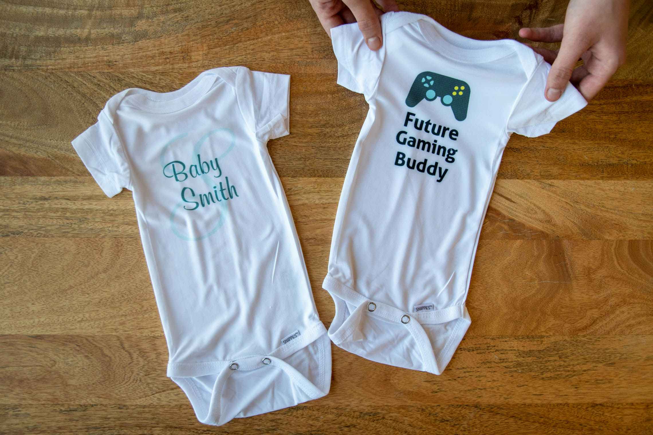 Two onesies, one with "baby smith" on it. The other with a gaming system controller and words, "future gaming buddy