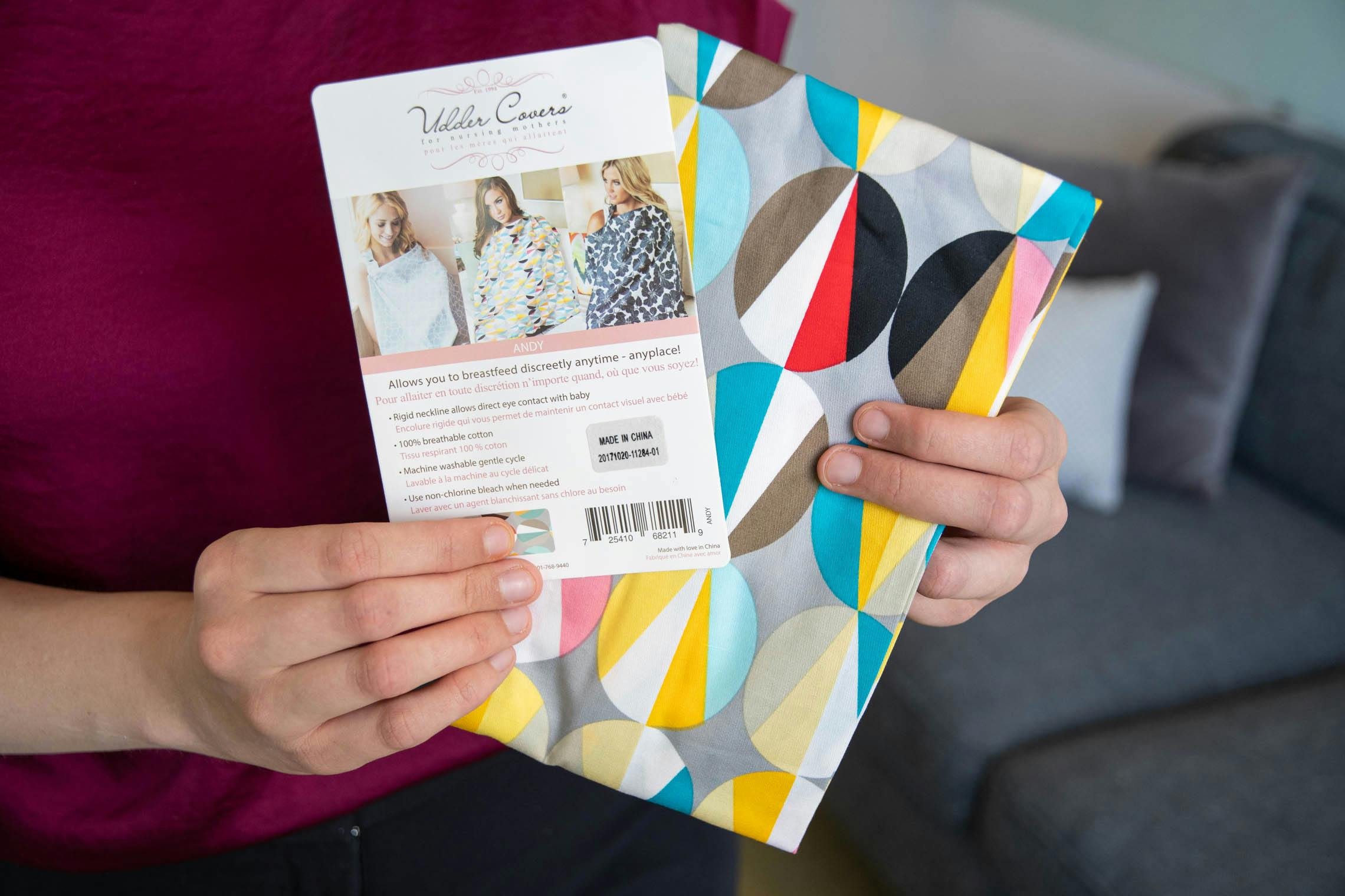 A person holding a nursing cover and card from Udder Covers.