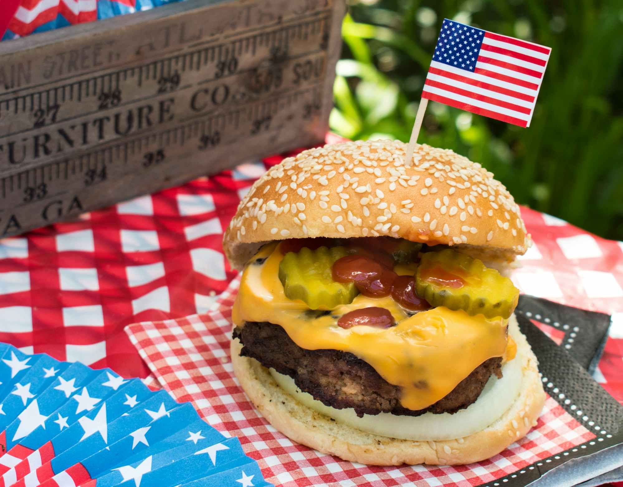 A large hamburger on a table with some Americana decor and a small American flag toothpick in the bun