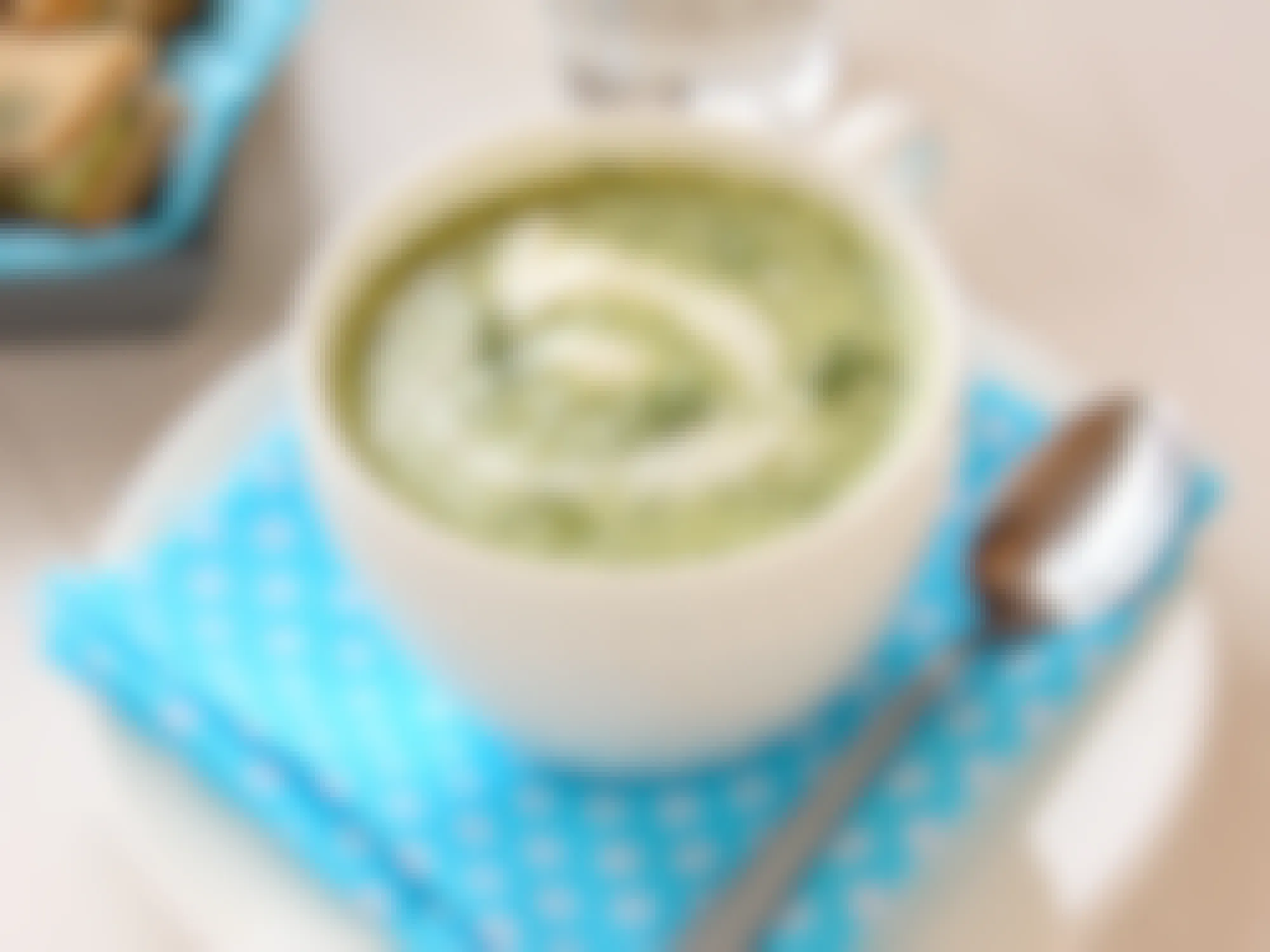 A small bowl of cold cucumber soup on a table with a spoon