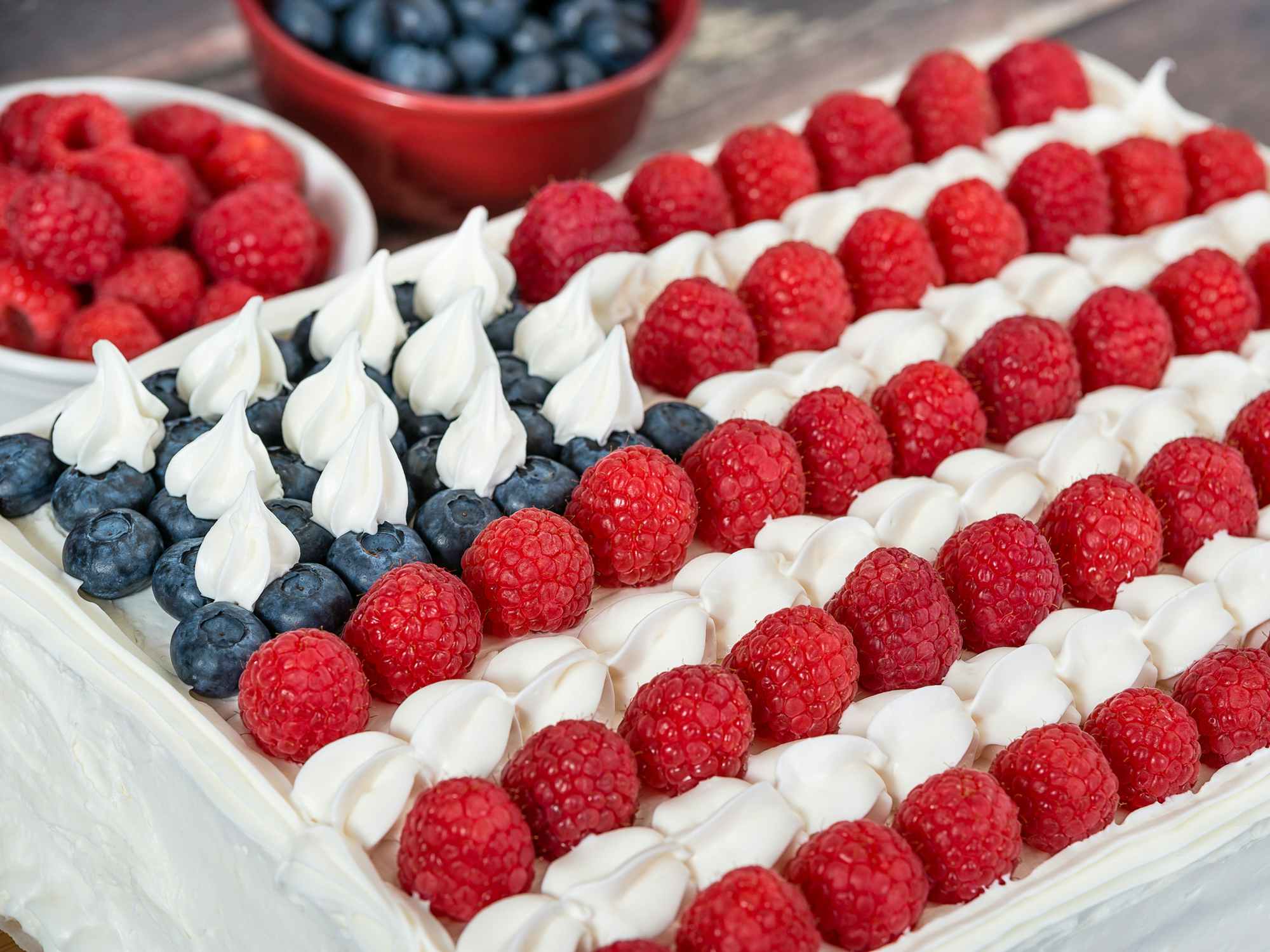 Patriotic, red white and blue, American flag cake. Fresh blueberries and raspberries in the background