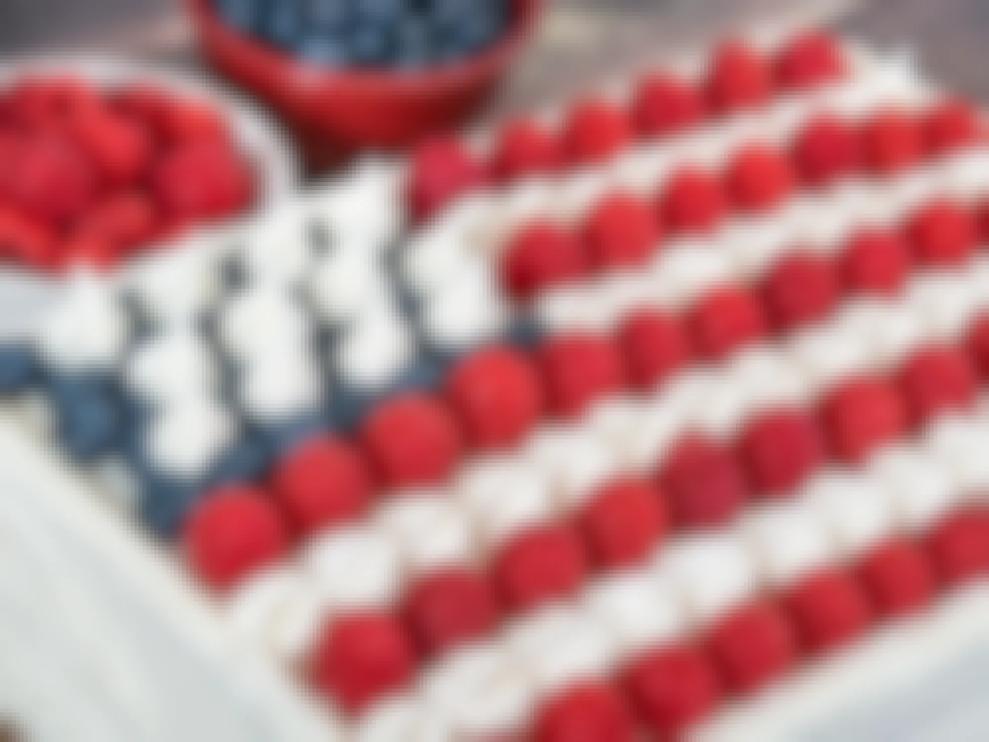 Patriotic, red white and blue, American flag cake. Fresh blueberries and raspberries in the background