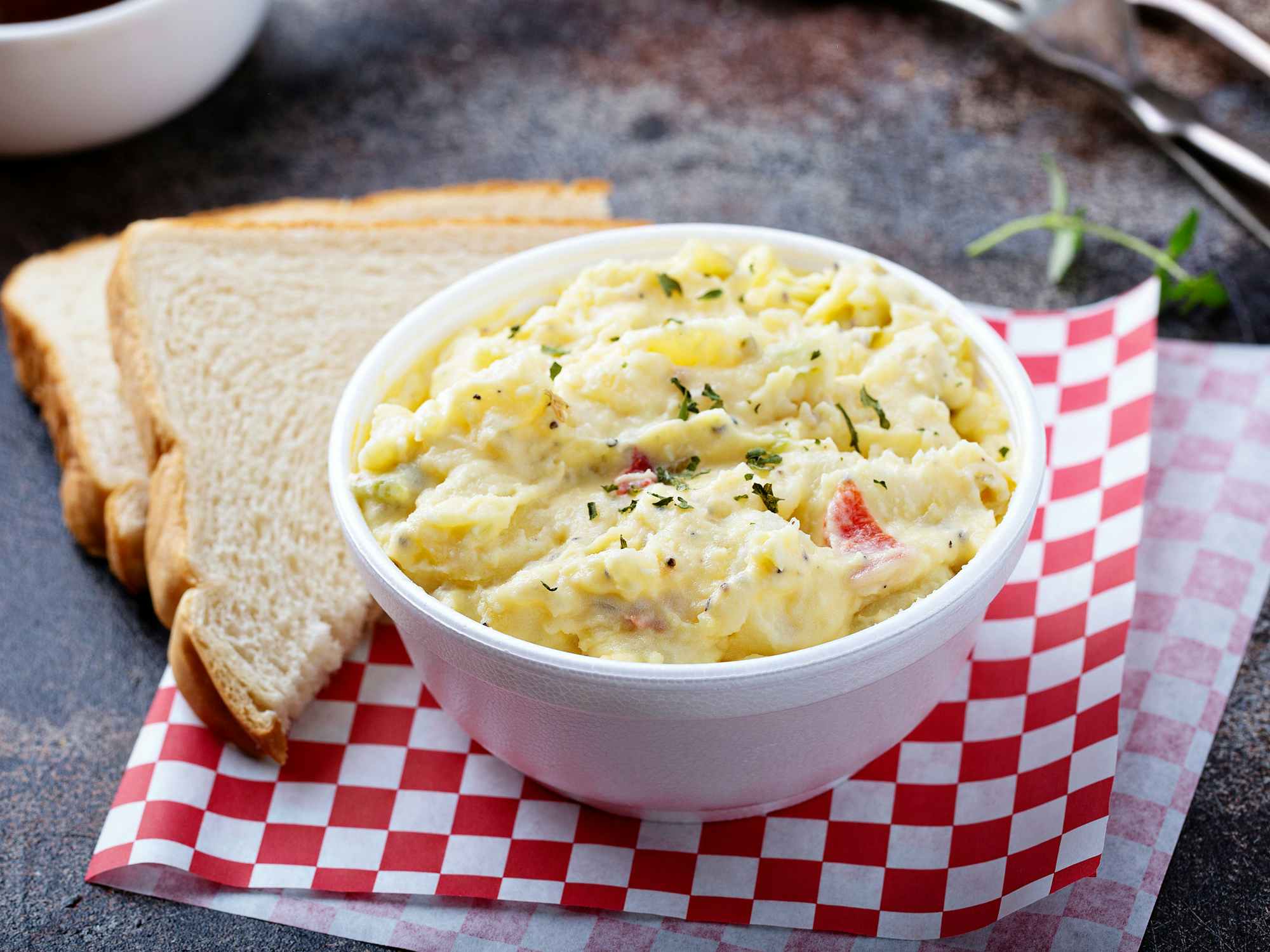 A bowl of potato salad next to some slices of bread