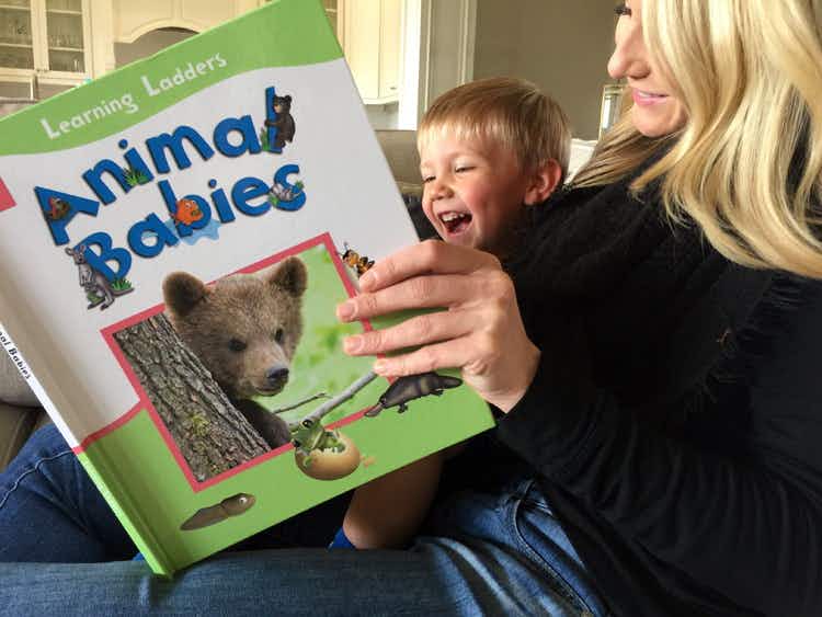 A woman reading an animal to a small boy who is smiling and laughing.