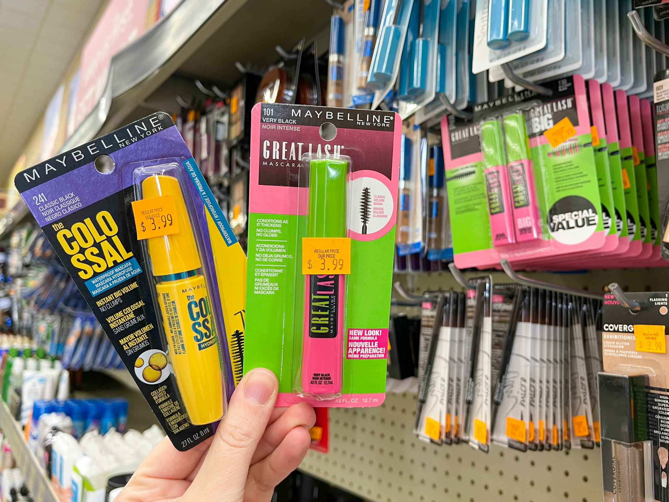 A person holding two package of Maybelline mascara in the cosmetics section at Grocery Outlet