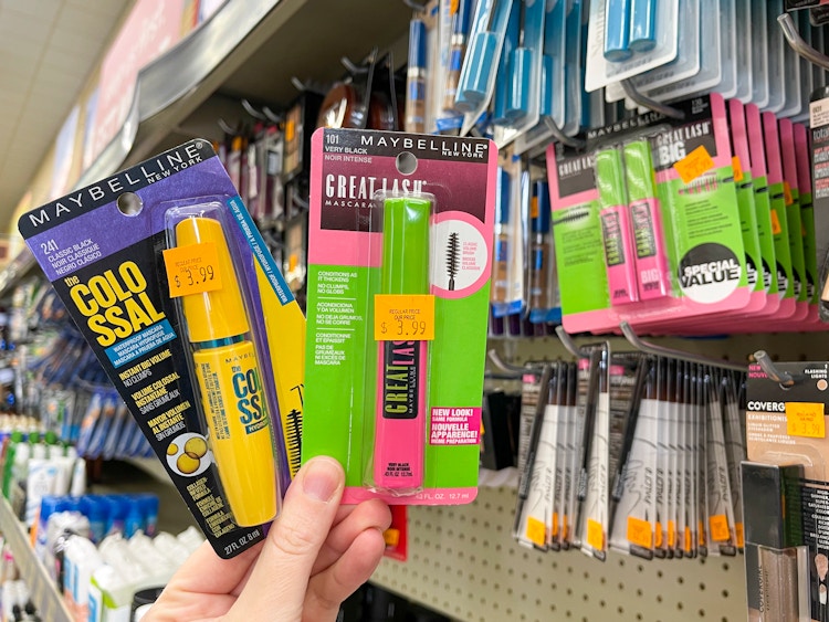 A person holding two package of Maybelline mascara in the cosmetics section at Grocery Outlet