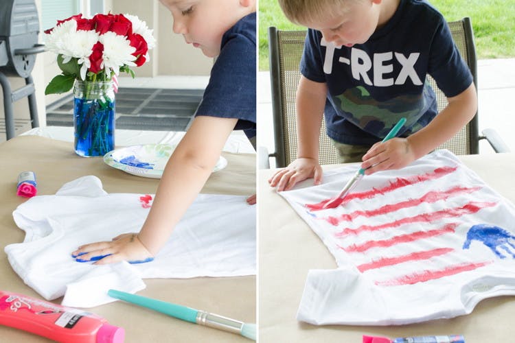 A child putting a blue paint handprint onto a white t-shirt and painting red stripes to make the shirt look like an American flag.