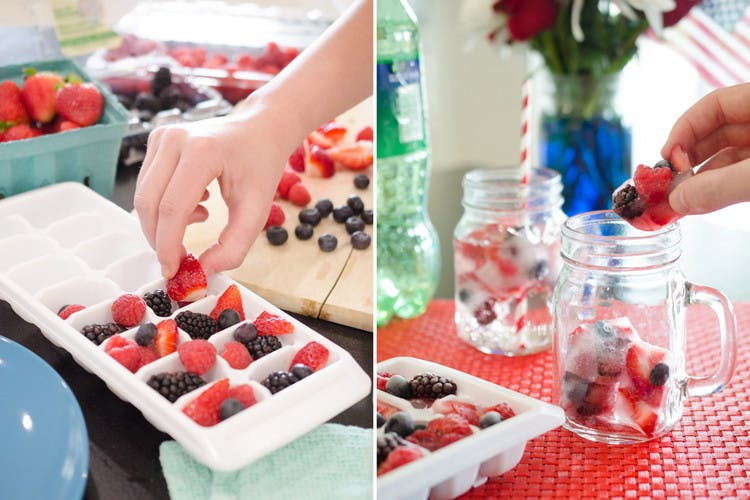 A person's hand taking frozen berries out of an ice tray and putting the berry ice cubes in drink glasses.