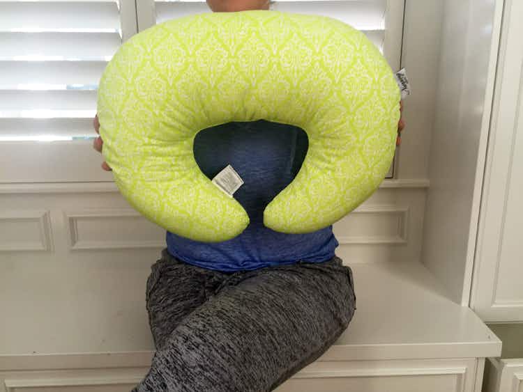 A woman in sweatpants holding up a lime green nursing pillow.
