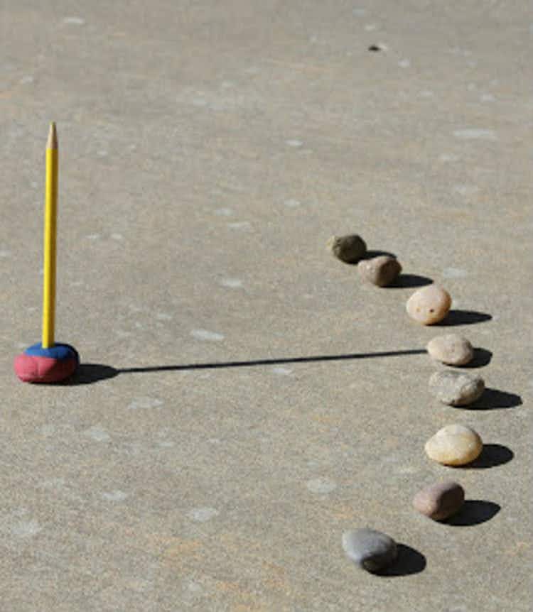a pencil and clay on the concrete to build a sundial with a half circle of rocks