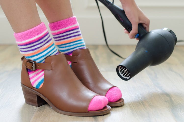 Someone stretching a pair of tight shoes by wearing thick socks and blow-drying the tight area.