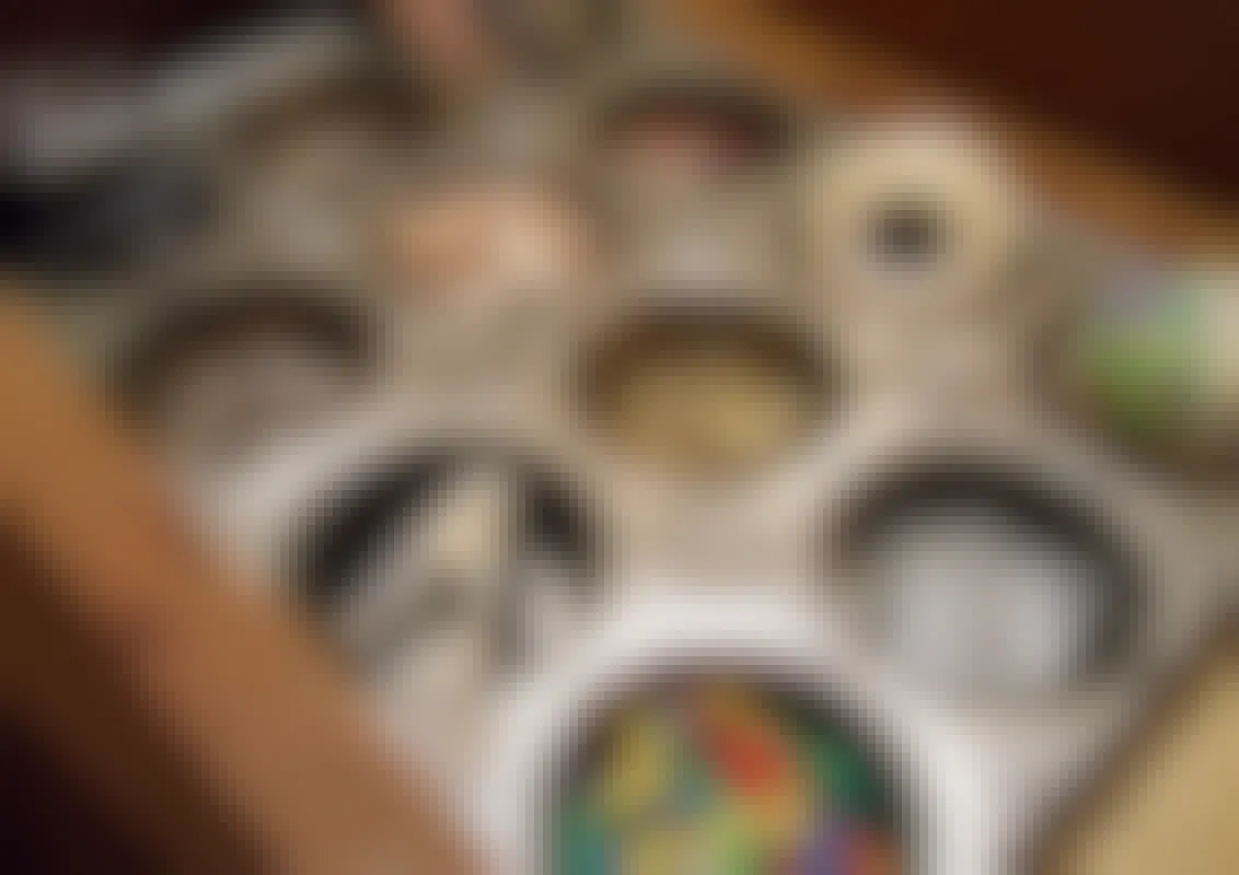A close-up of a muffin tin that is being repurposed to organize different school and office supplies like paperclips, tacks, binder clips, rubber bands, tape, and more.