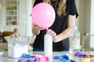 A person holding a balloon on the top of a bottle.