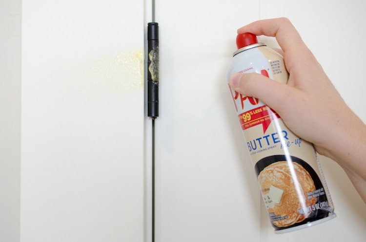someone spraying cooking spray on cabinet