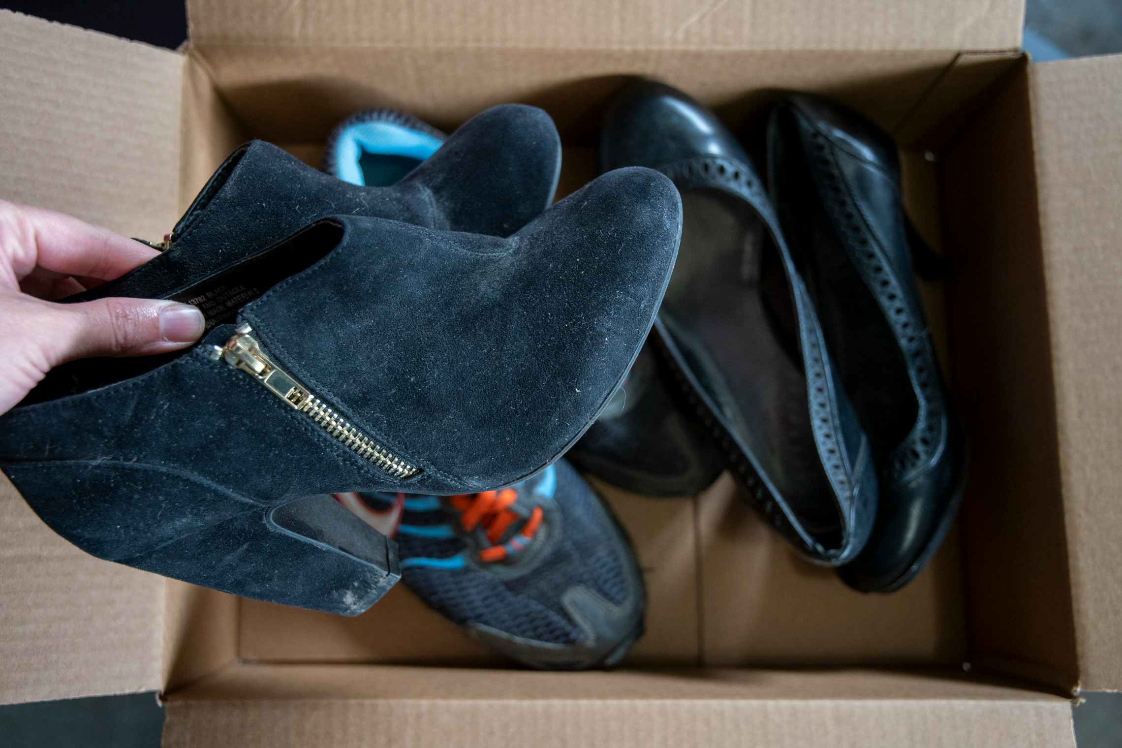A person putting a pair of heels into a cardboard box with two other pairs of shoes