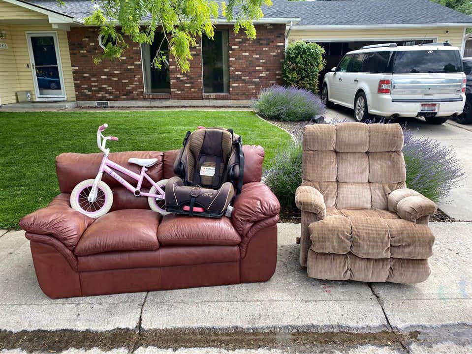 Safe, recliner, car seat, and bike sitting on the curb in front of someones house.