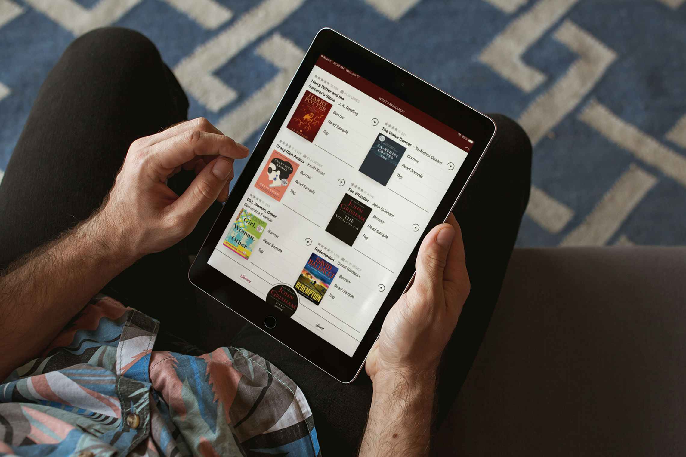 A man sitting on a couch looking at an ipad with a digital library app open on the screen.