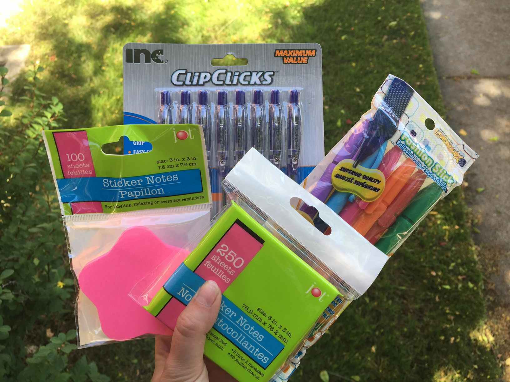 A person holding packages of pens and sticky notes in one hand while walking outside.