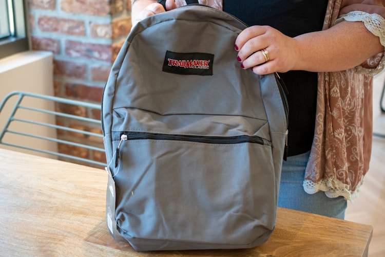 A person holding a backpack and zipping it closed.