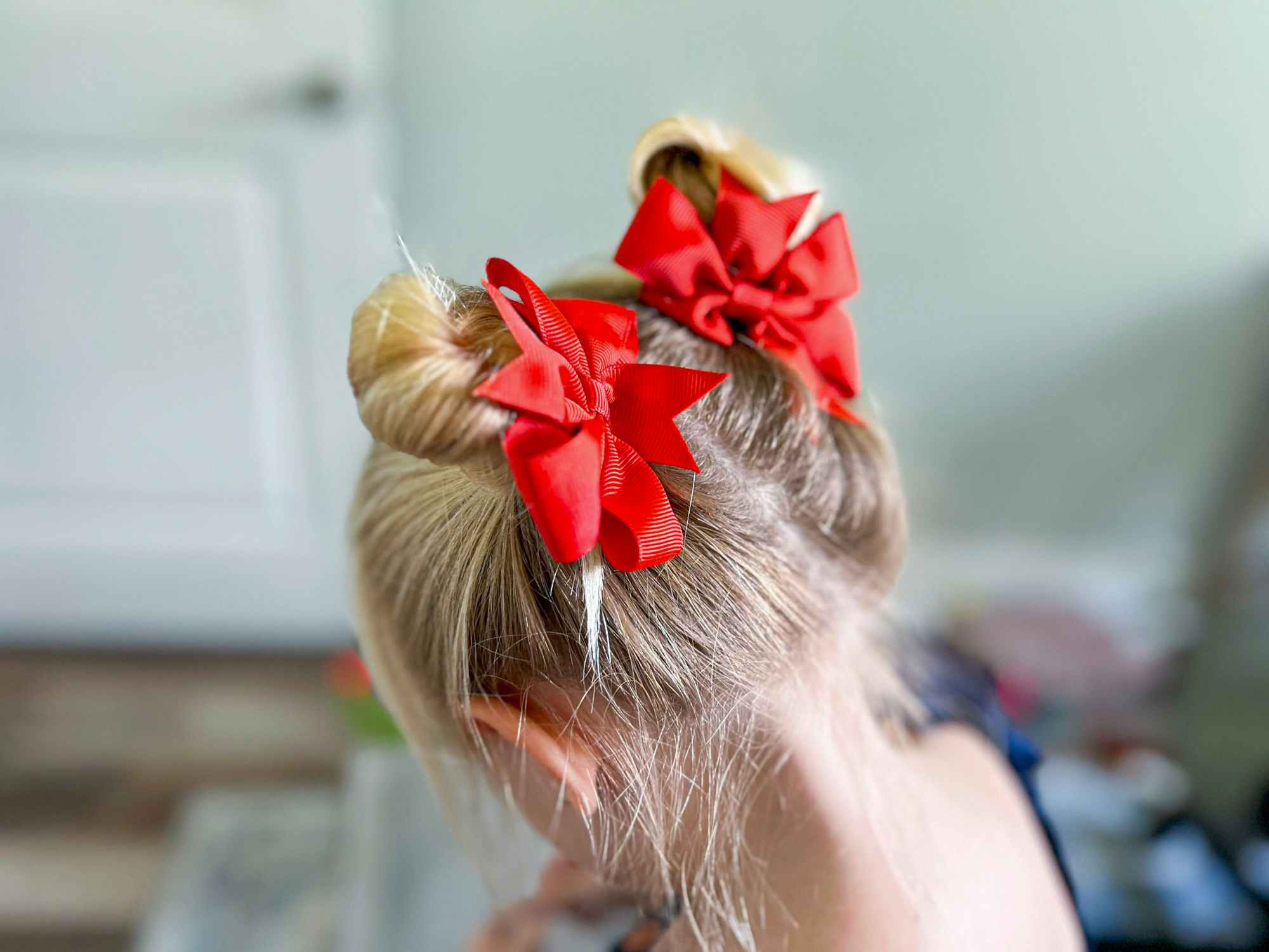 A little girl showing off her hairstyle - two high buns with big red bows