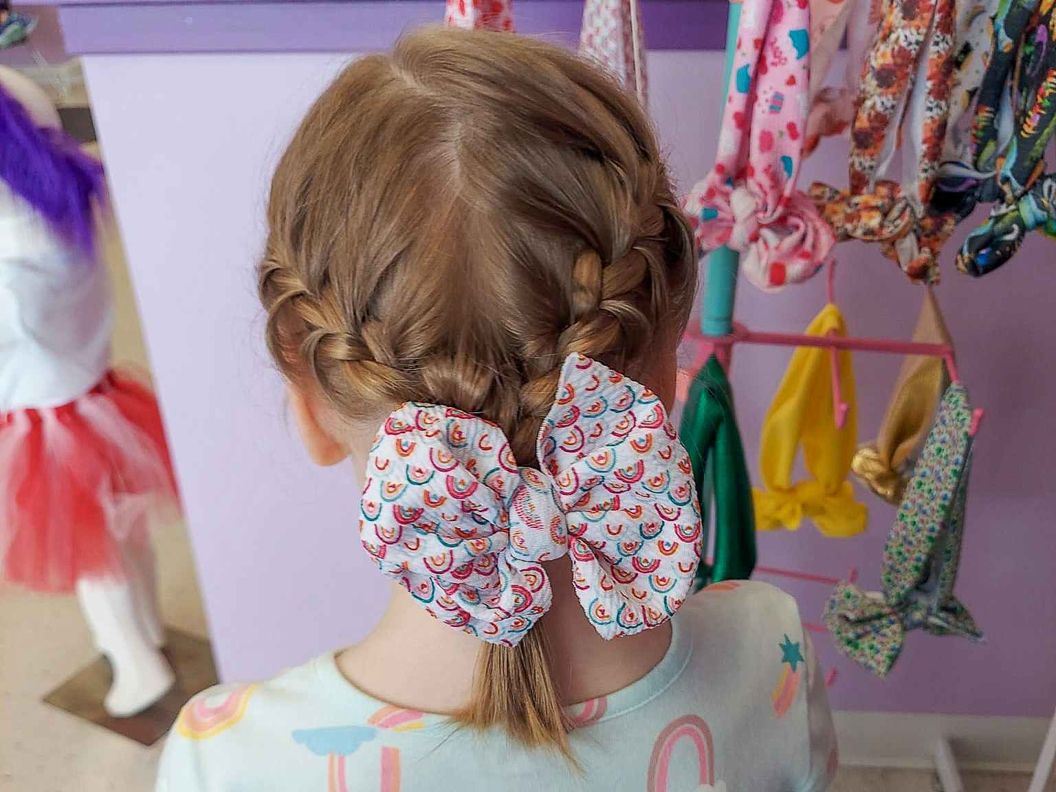 A young girl with two french braids joined into a poytail with a bow