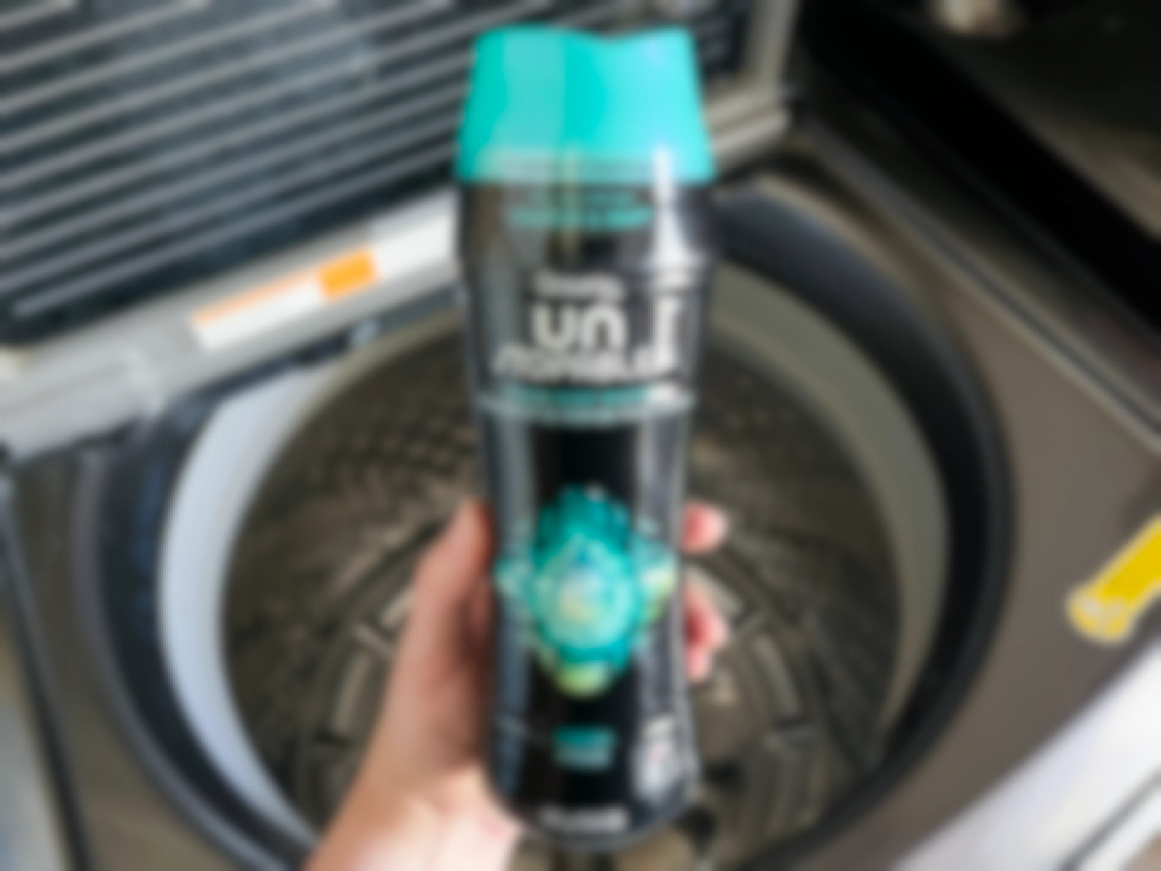 A person's hand holding a bottle of Downy Un Stopables laundry scent boost over an open washing machine.