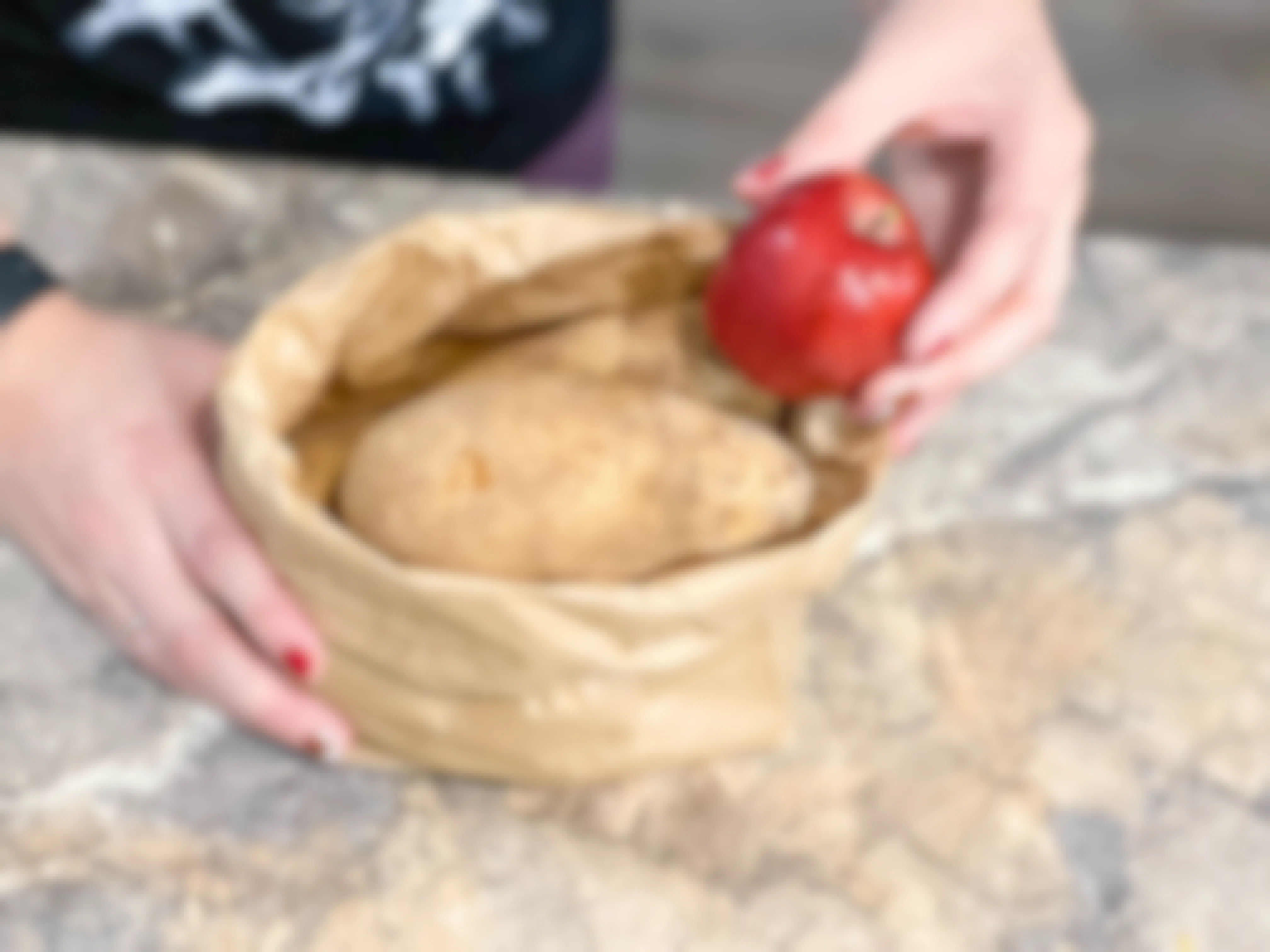 potatoes in a bag with an apple being added