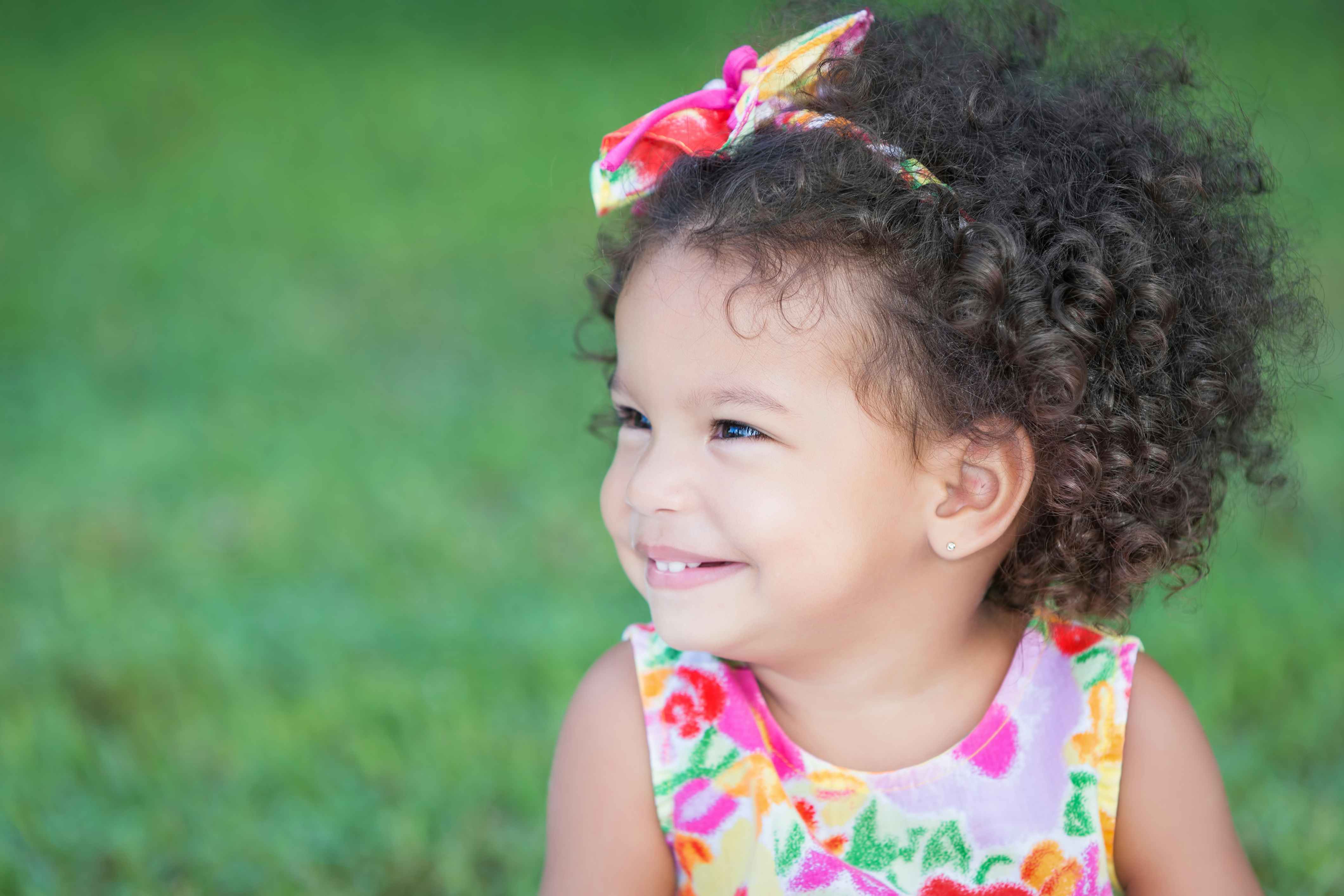 A little girl with natural curls sitting outside smiling.