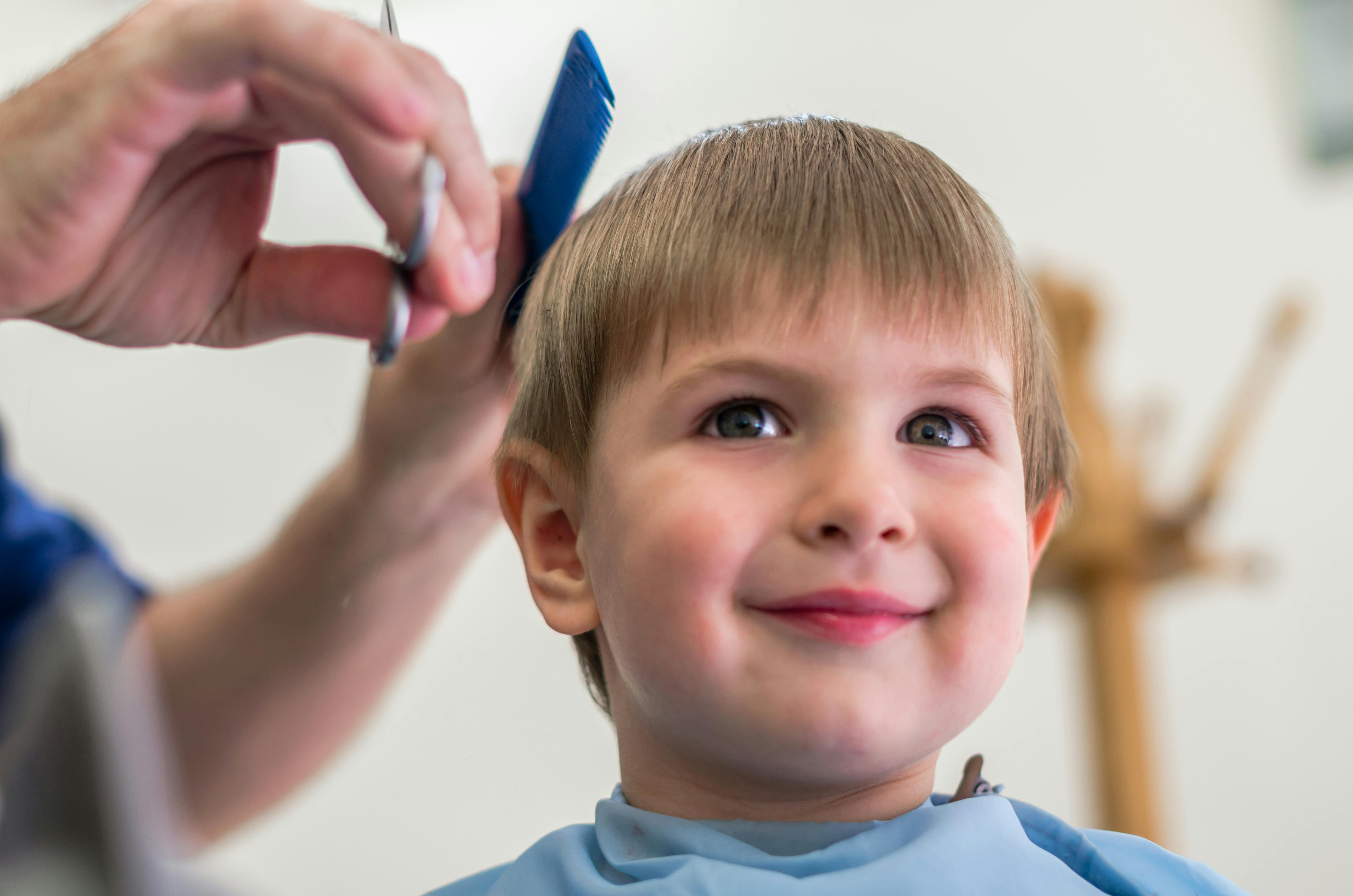 A little boy smiling while having his hair cut.