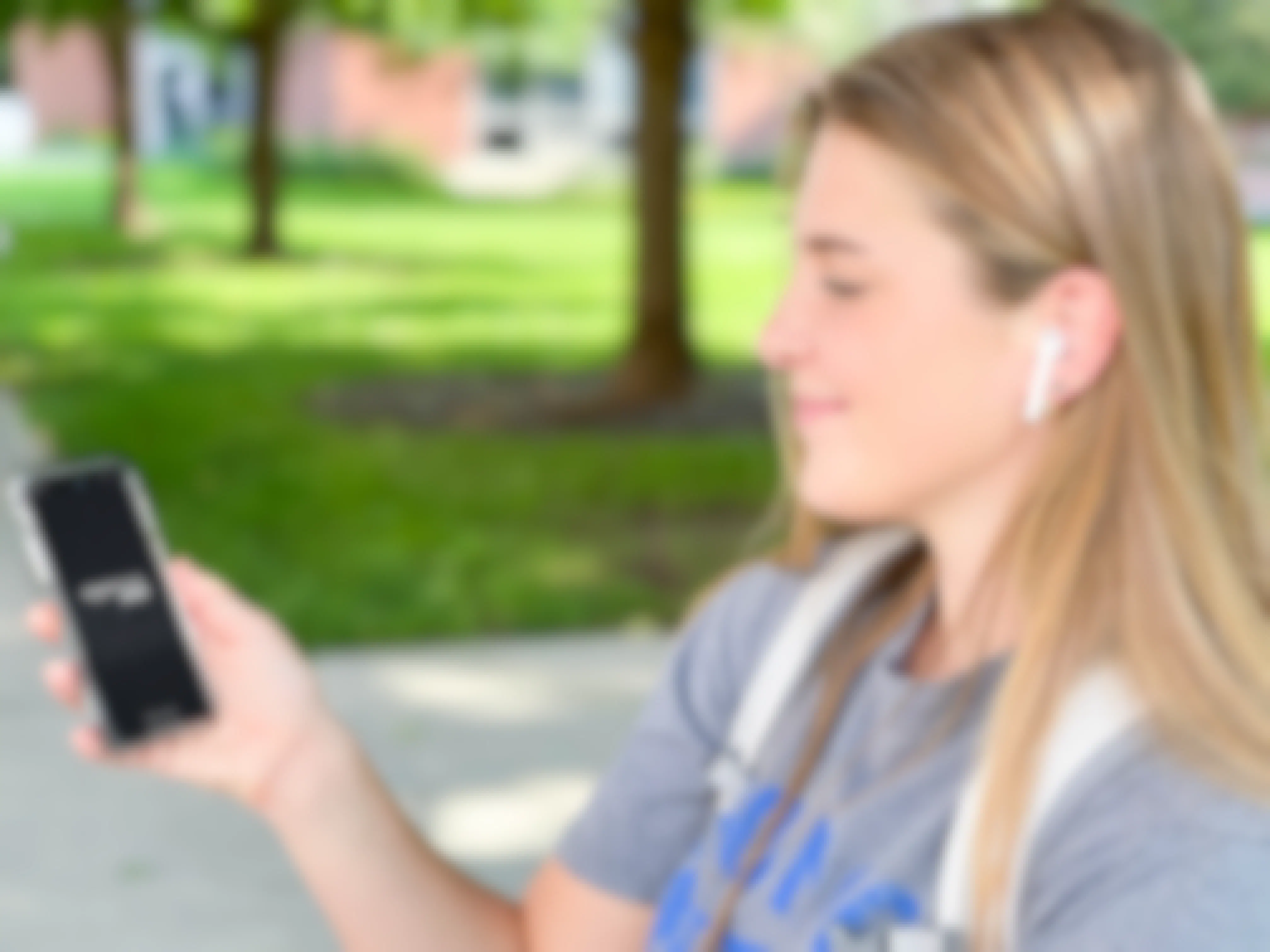 A college student with Airpods in her ears and the Amazon Music app start screen displayed on her phone.