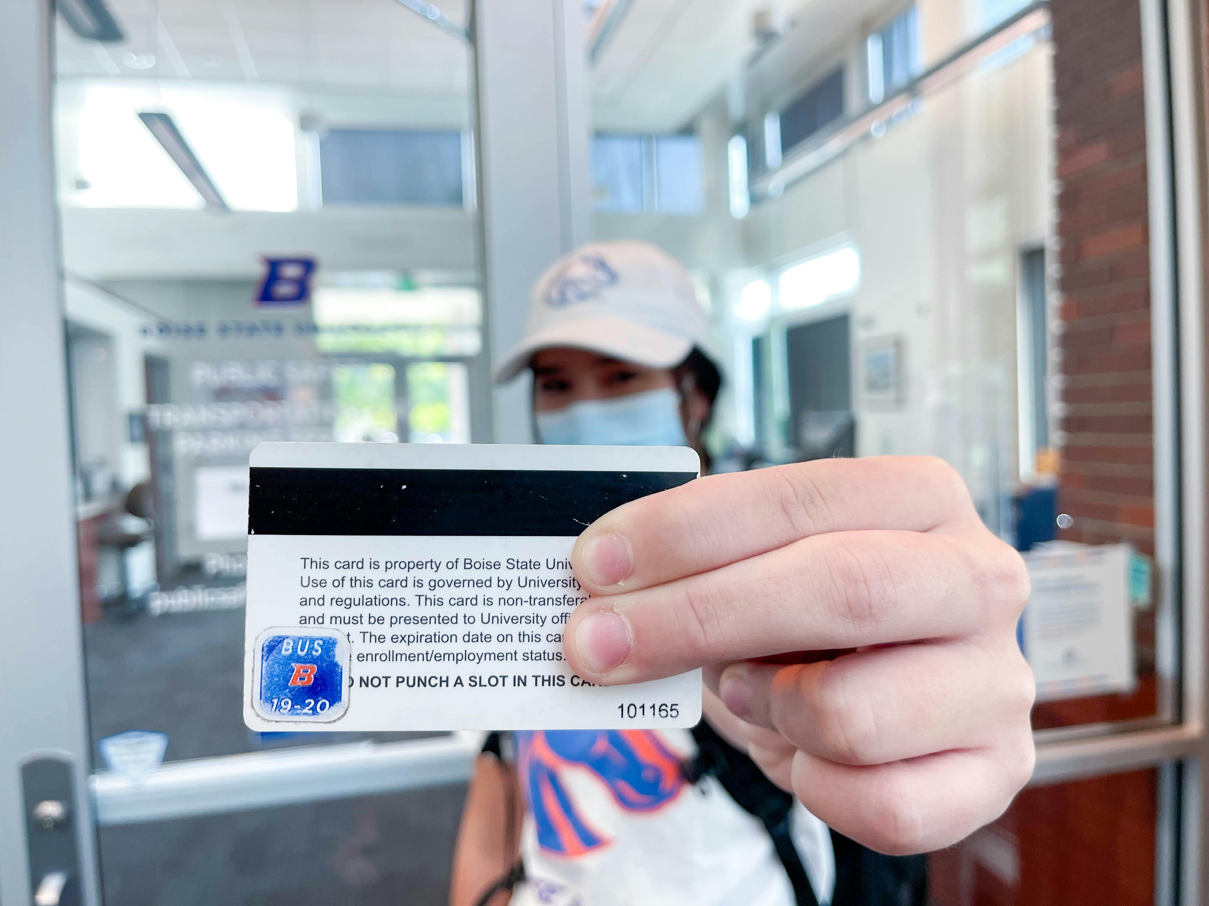 A college student holding up their student ID, showing a bus sticker on the back.