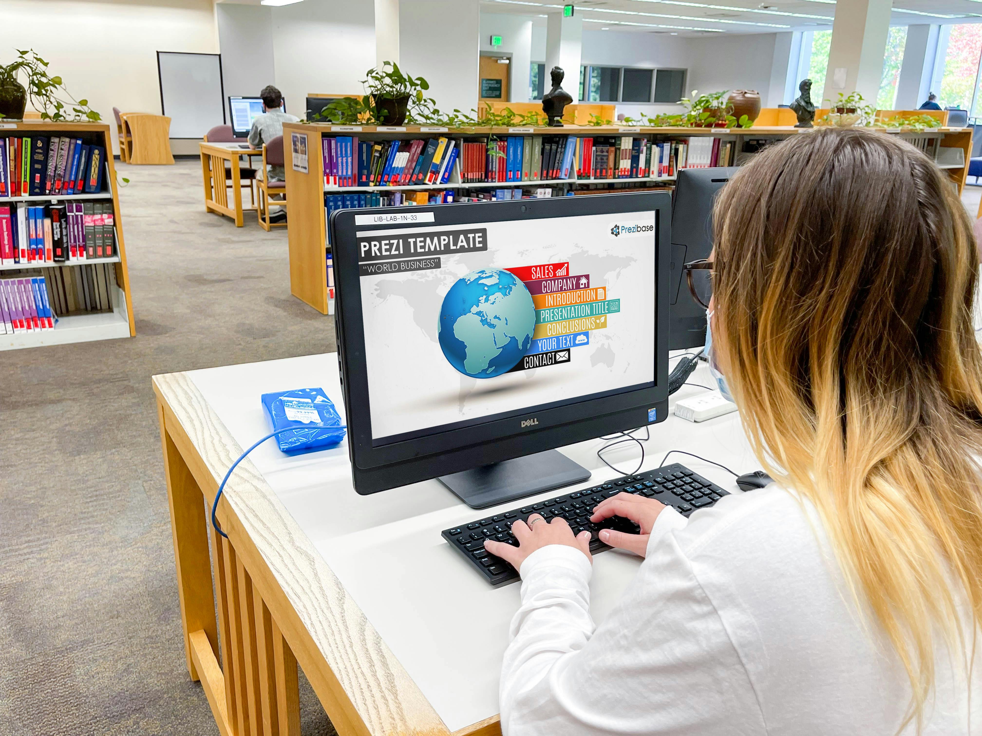 A college student sitting at computer in a library looking at the Prezi Template webpage.